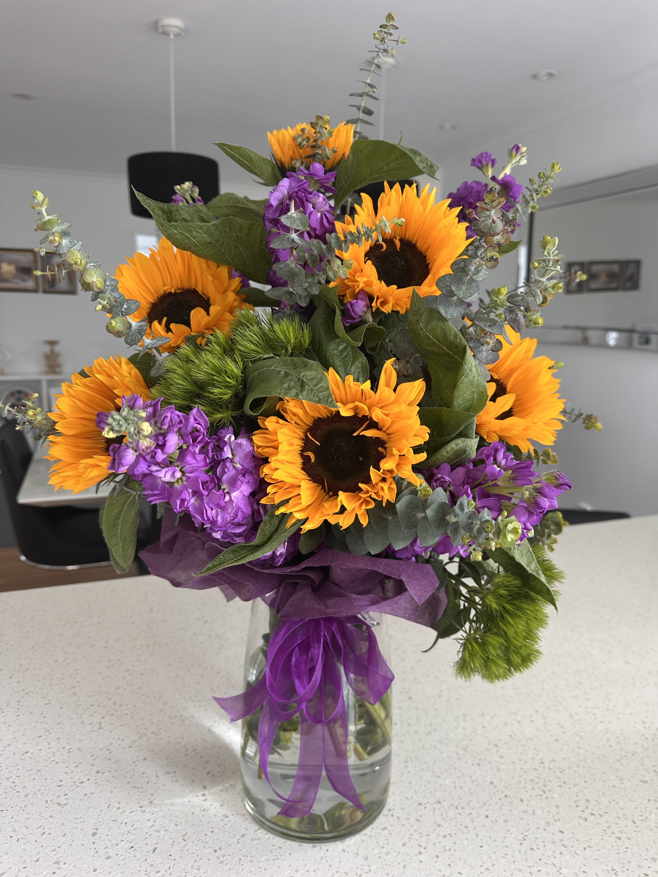 Sunflowers in glass vase with purple toned flowers